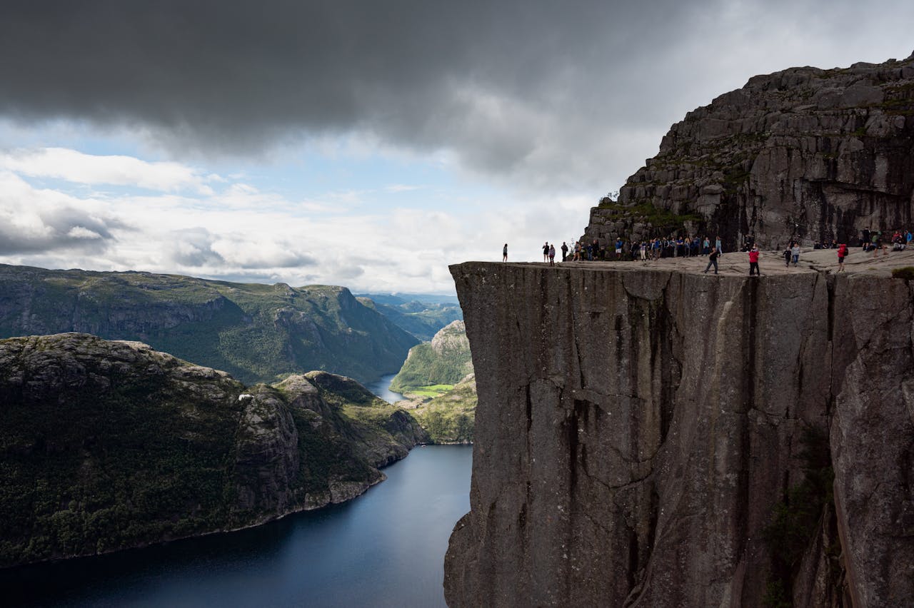 Photo showing dramatic view of hikers on Preikestolen, a high cliff face overlooking a stunning fjord in Norway.